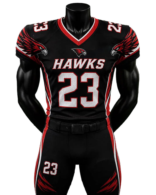 A black football uniform set displayed on a black mannequin torso against a green grass-like background. The jersey and pants are black with red and white accents, featuring the word HAWKS across the chest, the number 23 on the front and thigh, eagle head graphics on the shoulders, and a hawk logo on the chest.